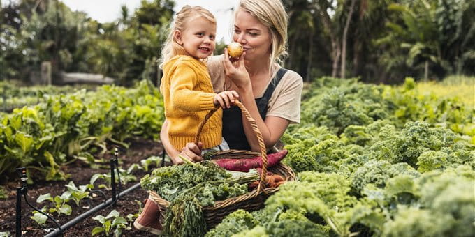 Eine Frau und ein Kind halten einen Korb mit Gemüse in einem Garten. Eine Frau und ein Kind halten einen Korb mit Gemüse in einem Garten.