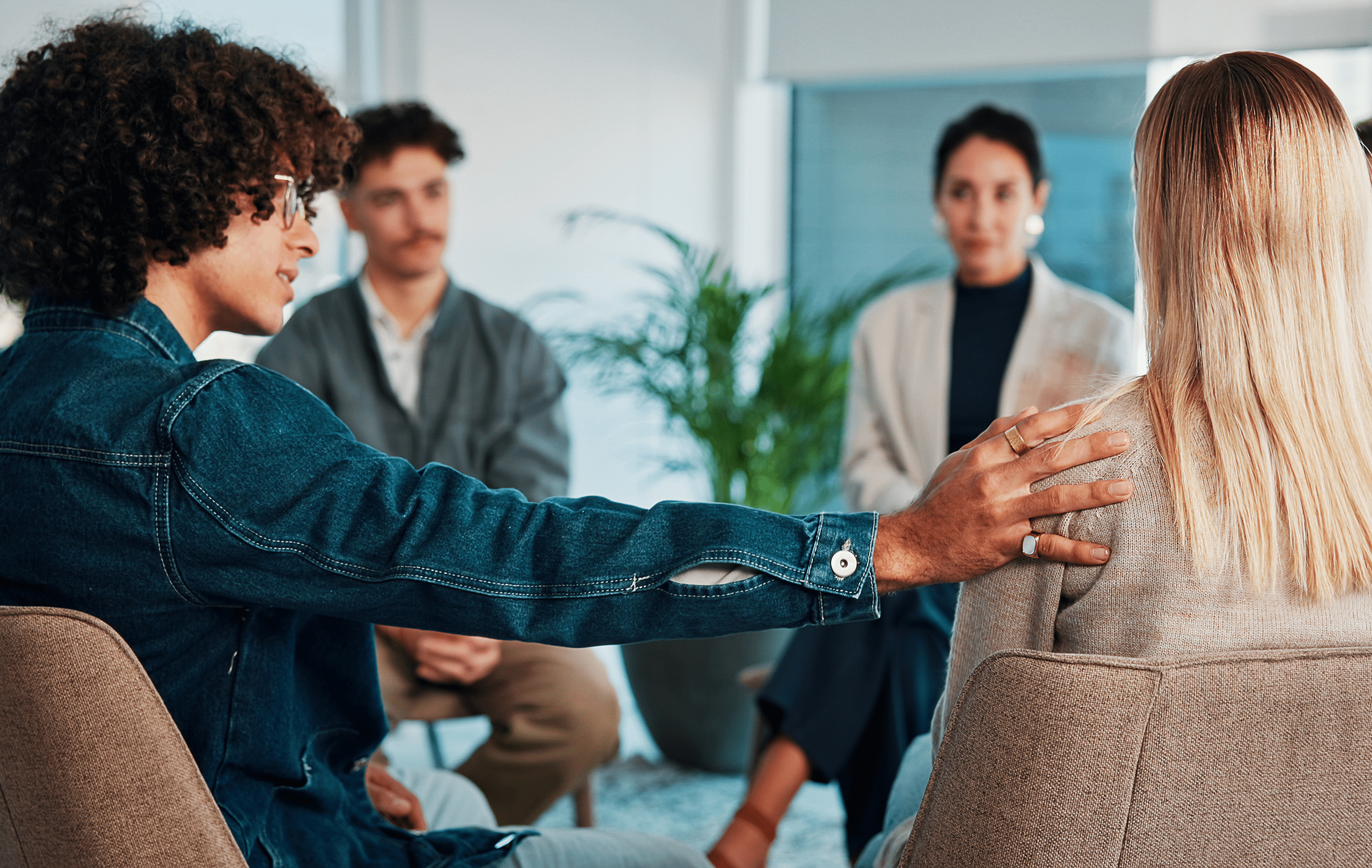 A group of people in discussion. One person is placing a hand on another person's shoulder. A group of people in discussion. One person is placing a hand on another person's shoulder.