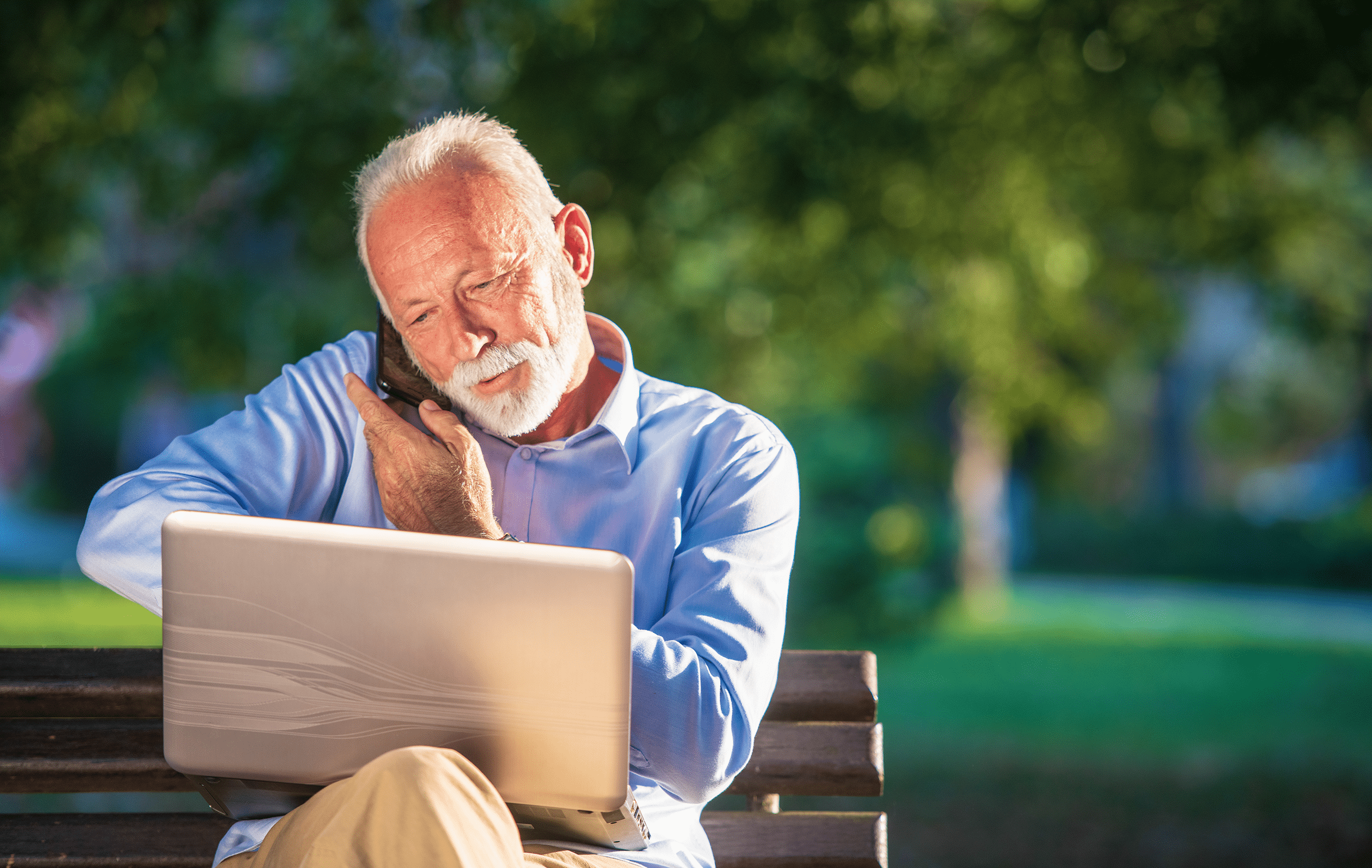 Vecchio signore seduto sulla panchina del parco, telefonando e avendo il computer portatile in ginocchio. Vecchio signore seduto sulla panchina del parco, telefonando e avendo il computer portatile in ginocchio.