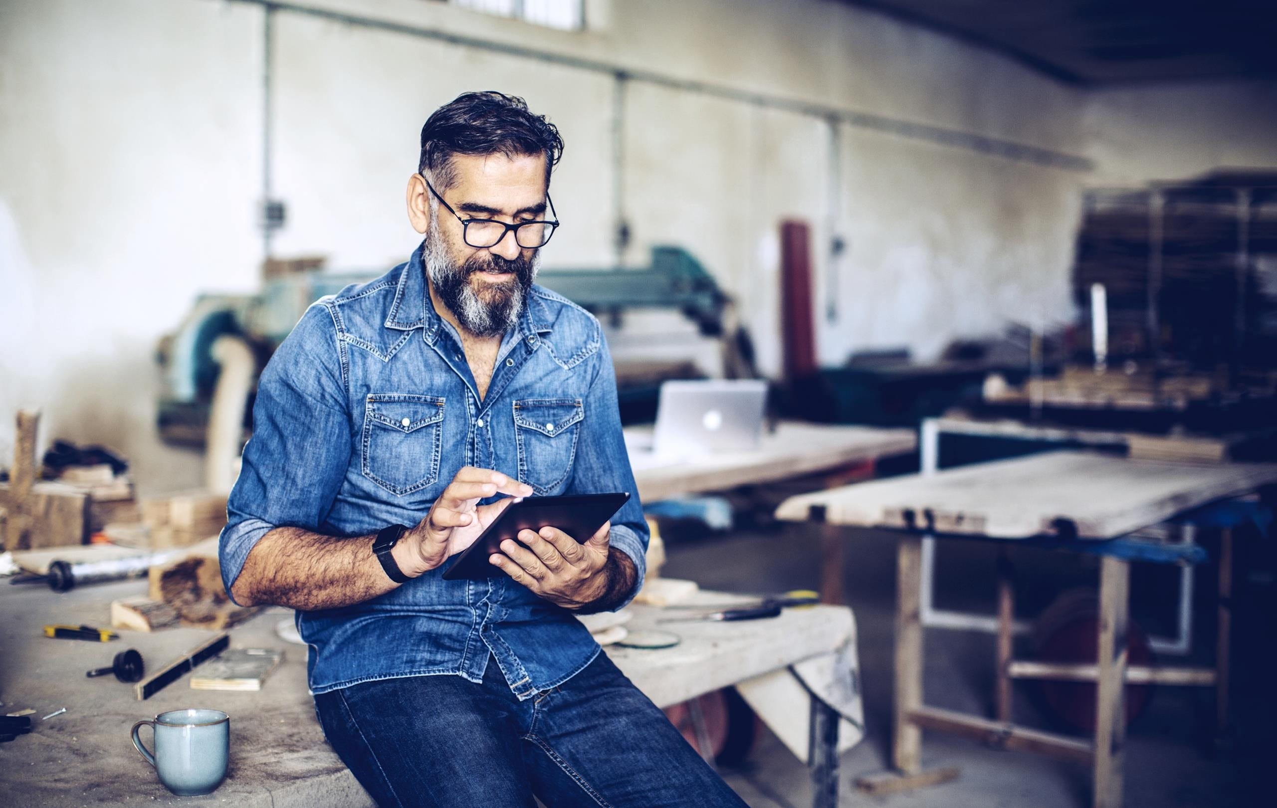 Mann sitzt auf Werkbank und schaut ins iPad