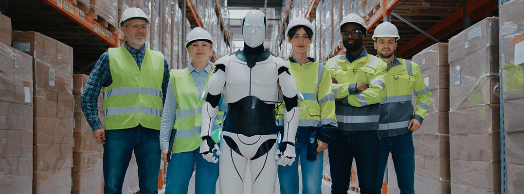 Eine Gruppe von Menschen in reflektierenden Westen steht neben einem humanoiden Roboter in einem Lagerhaus.