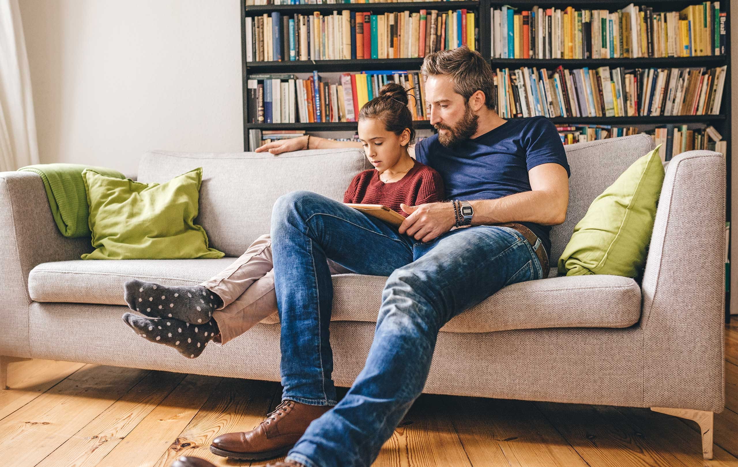 Father sits with daughter on the sofa and reads a book Father sits with daughter on the sofa and reads a book
