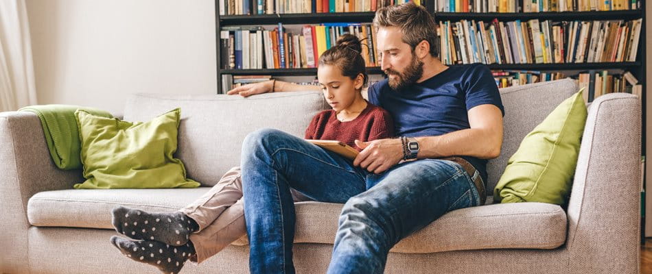 Il padre si si siede con la figlia sul divano e legge un libro